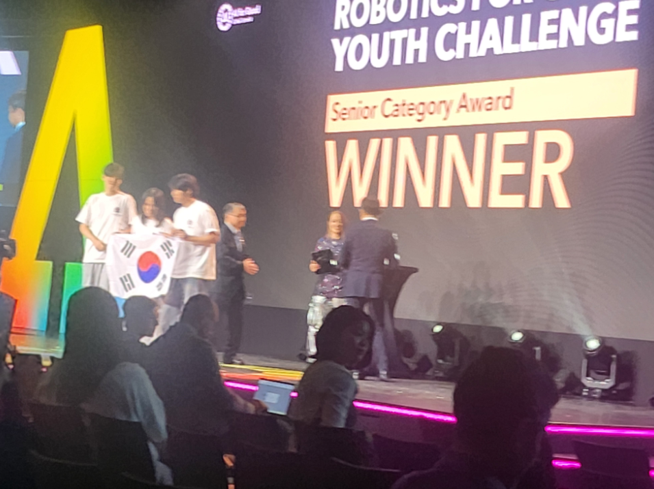 Robotics for Good Youth Challenge stage photo showing Senior Category Award Winner text and students holding the Korean flag.